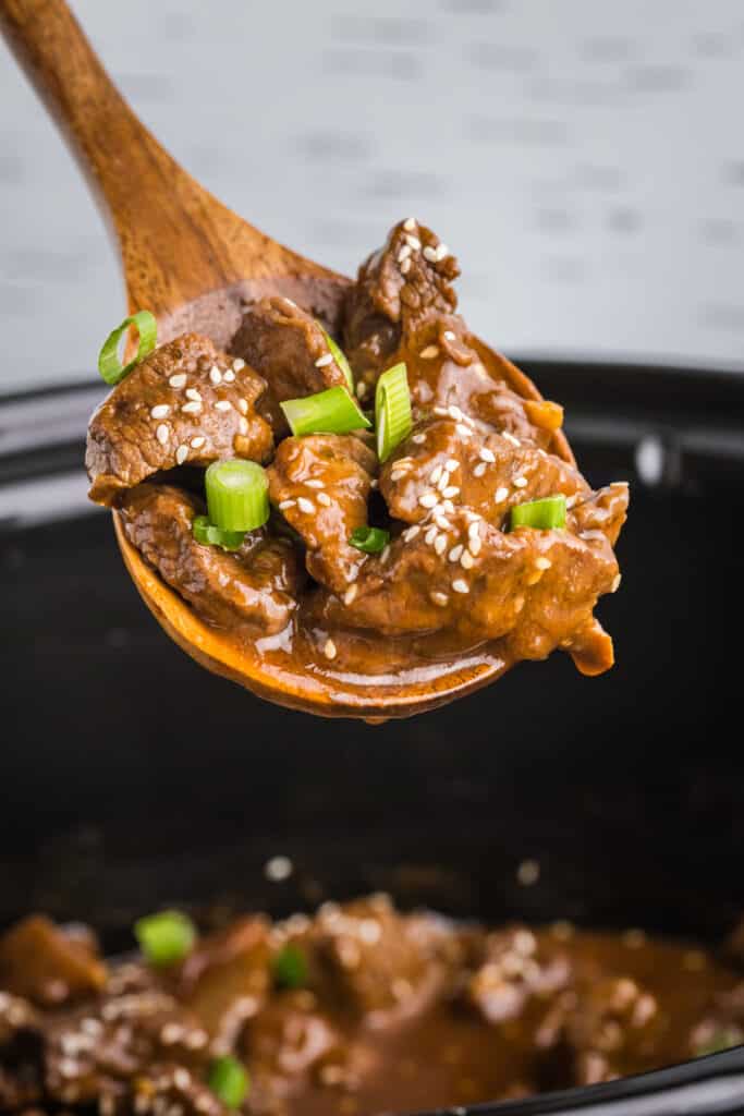 spoon lifting a scoop of crockpot honey garlic steak bites.