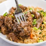 fork grabbing a bite of honey garlic steak bites on a plate with fried rice.