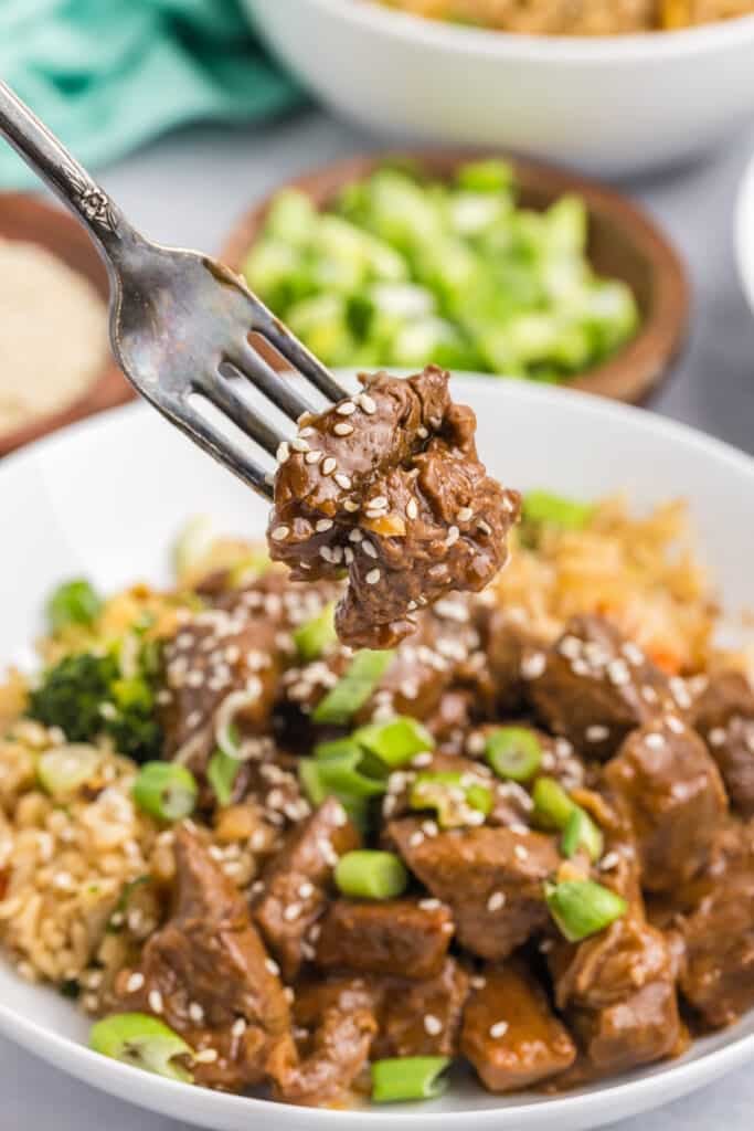 fork lifting a bite of steak bites from a plate with fried rice.