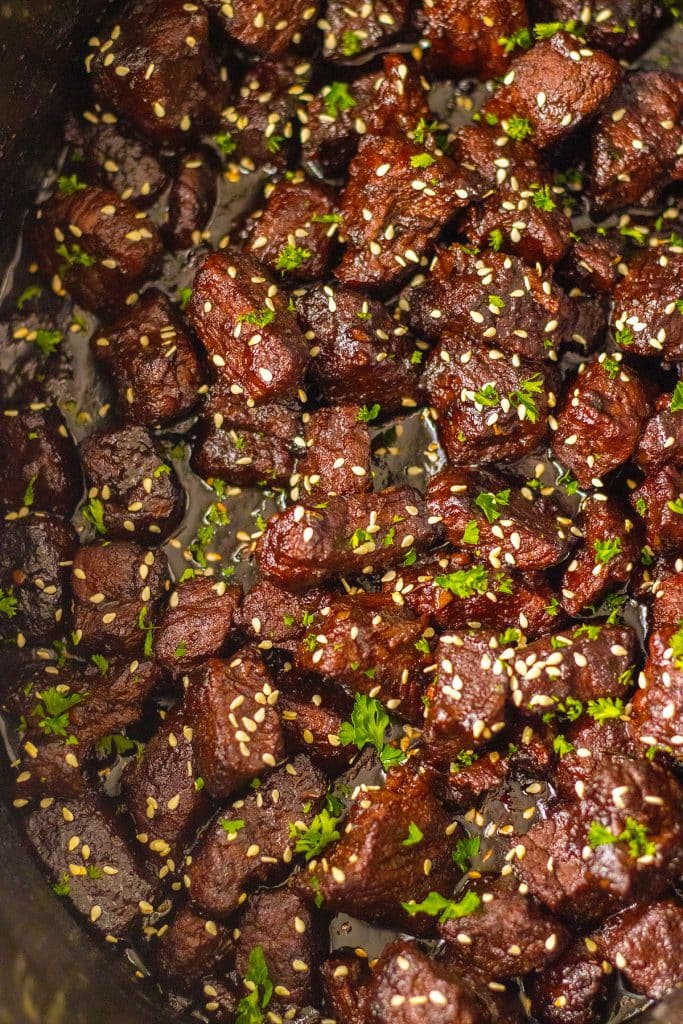 overhead shot of honey garlic steak bites sprinkled in sesame seeds in a slow cooker.