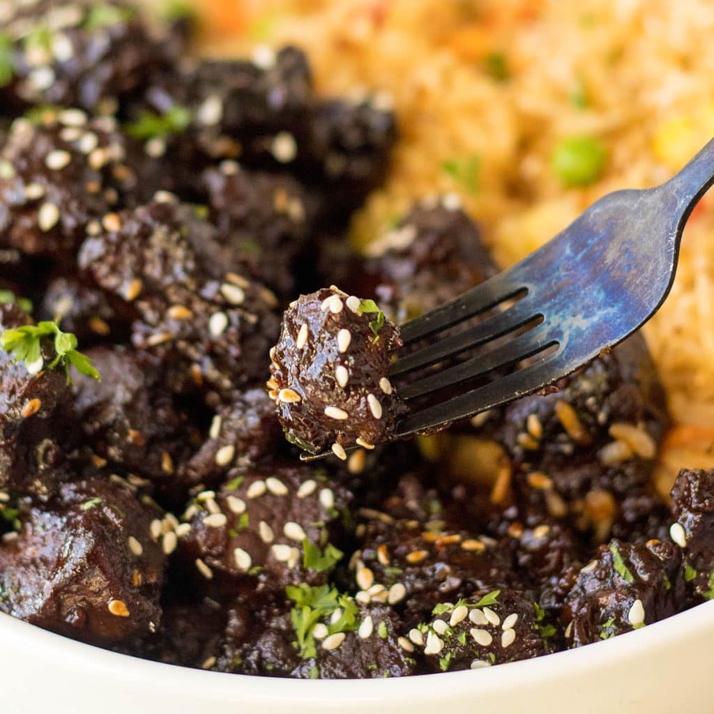 fork lifting a honey garlic steak bite from a bowl.