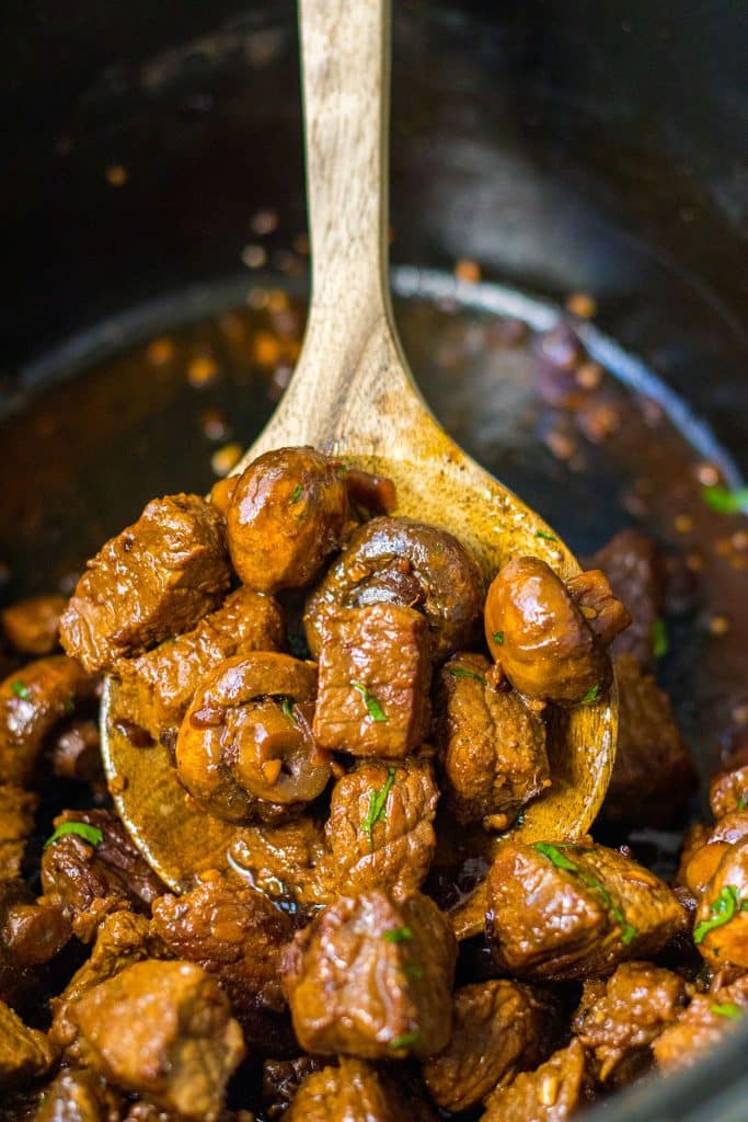 wood spoon scooping mushroom steak bites from a crockpot.