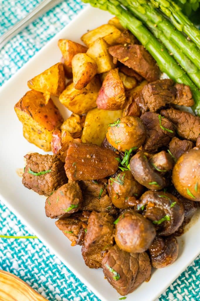 white plate with mushroom steak bites, roasted potatoes, and asparagus.