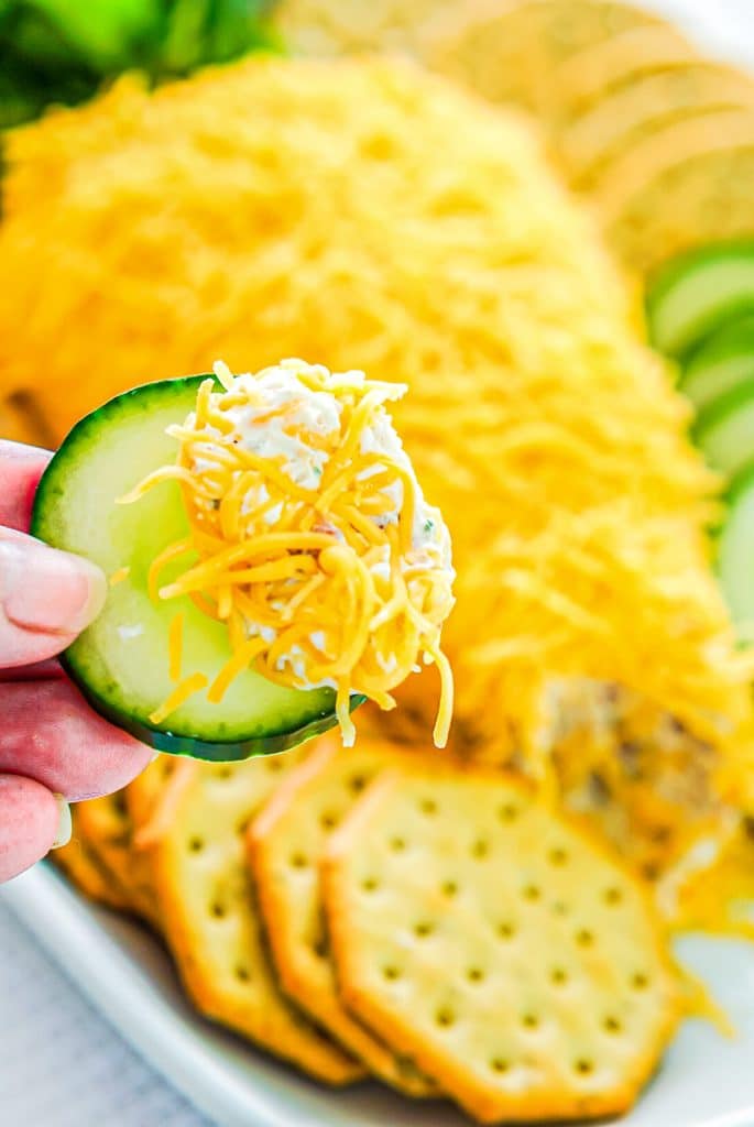 hand holding a cucumber dipped in cheese ball.