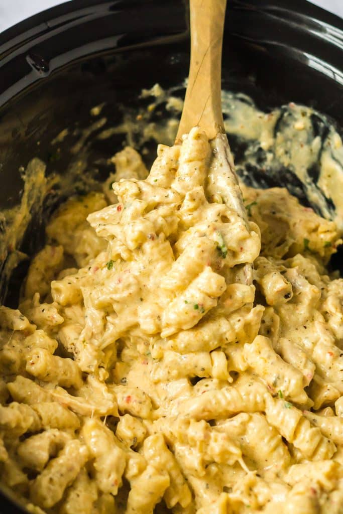 wooden spoon in a crockpot of chicken pasta.