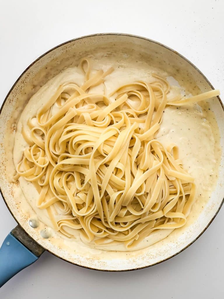 fettuccine noodles in a pan of alfredo sauce.