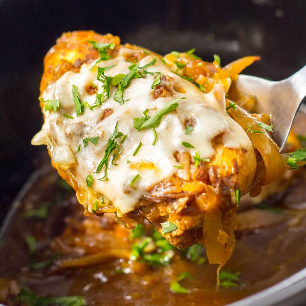 spoon lifting a cheesy french onion chicken breast from a crockpot.