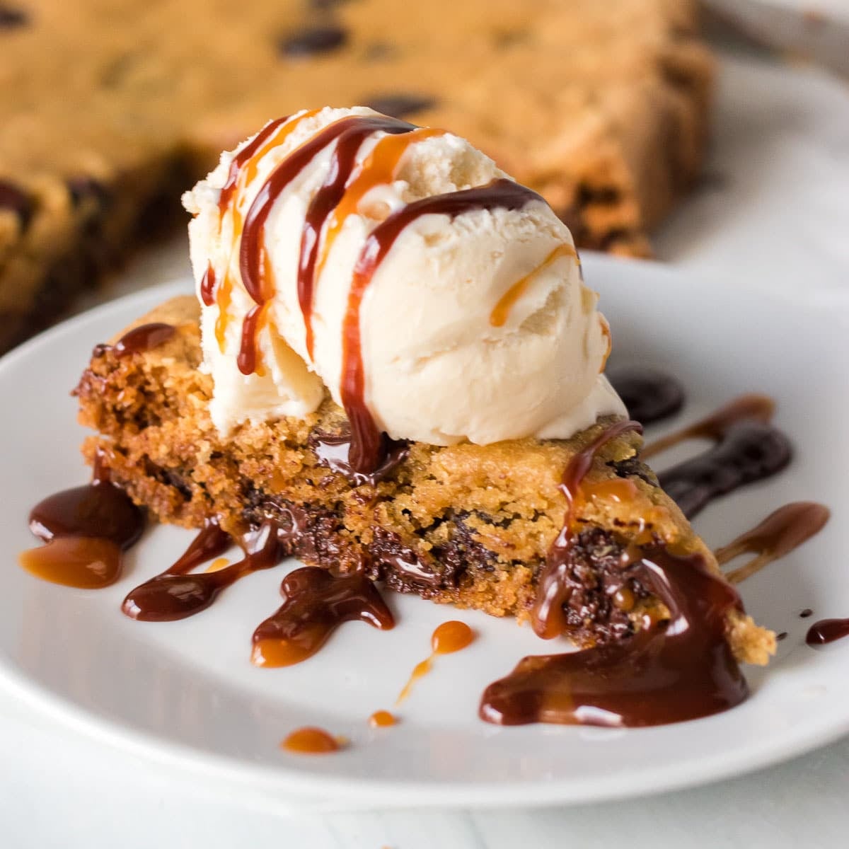 slice of chocolate chip cookie cake topped with ice cream and hot fudge.