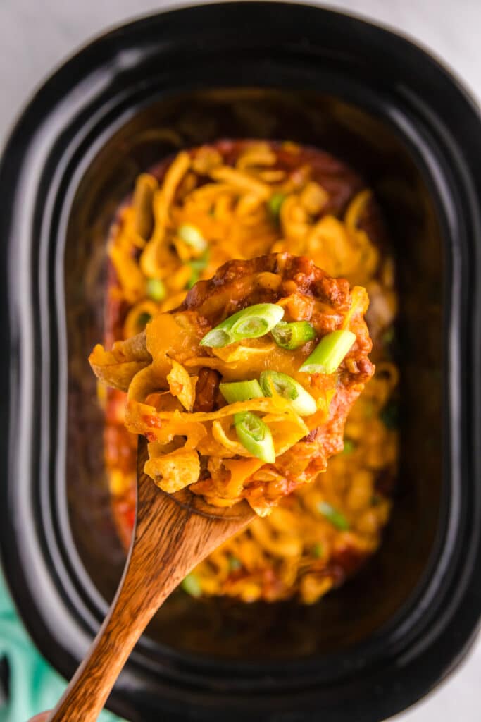 overhead shot of frito chili pie and a scoop in a slow cooker.