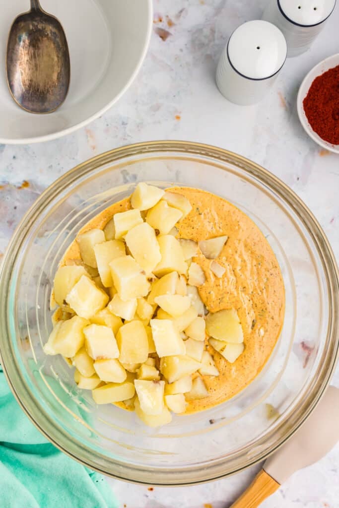overhead shot of diced potatoes & sauce in a glass mixing bowl.