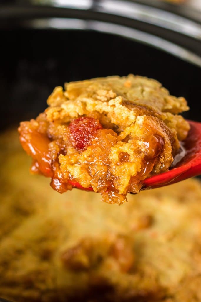 spoon lifting a scoop of pineapple dump cake from a slow cooker.