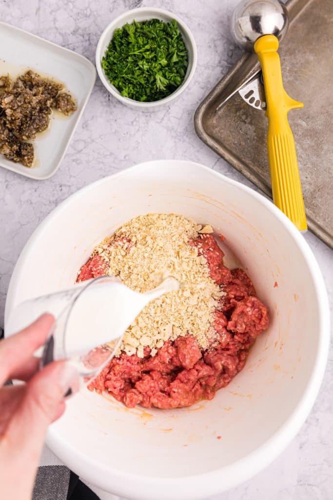 milk pouring into a meatball mixture.