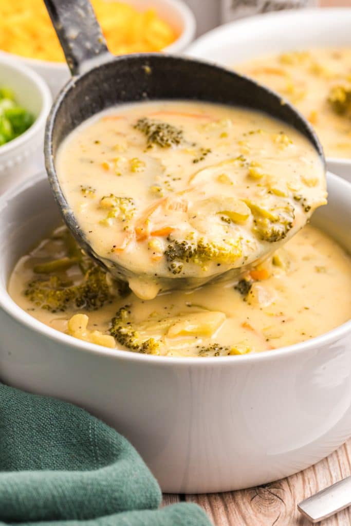 ladle scooping broccoli cheese soup into a soup bowl.