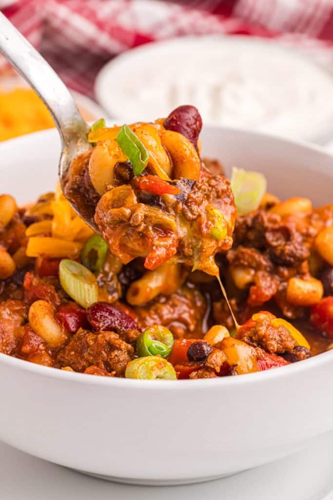 spoon lifting a bite of chili mac from a white bowl.