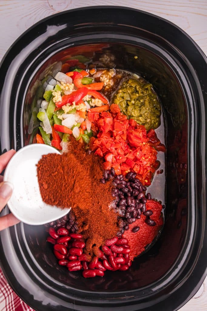 chili seasoning being sprinkled into a slow cooker of chili.