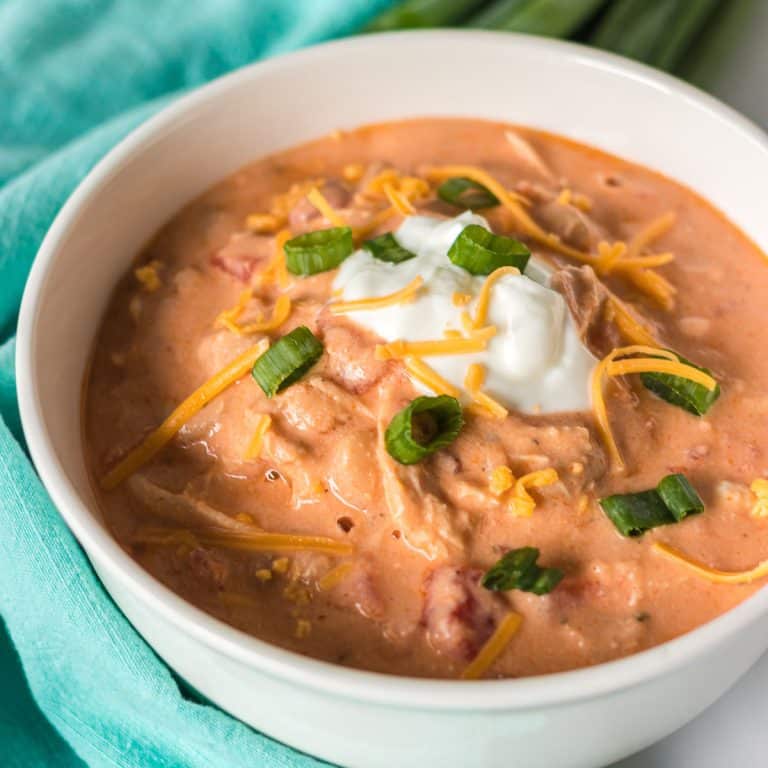 white bowl of buffalo chicken chili topped with sour cream, scallions, and shredded cheese.