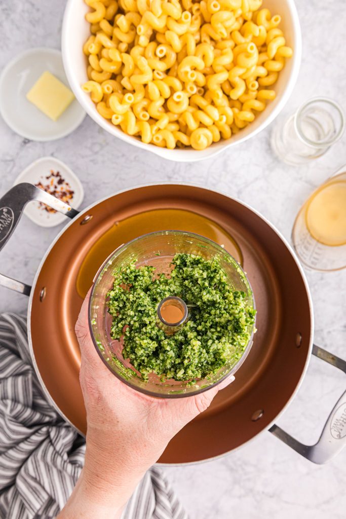 overhead shot of hand holding a food processor full of pesto.