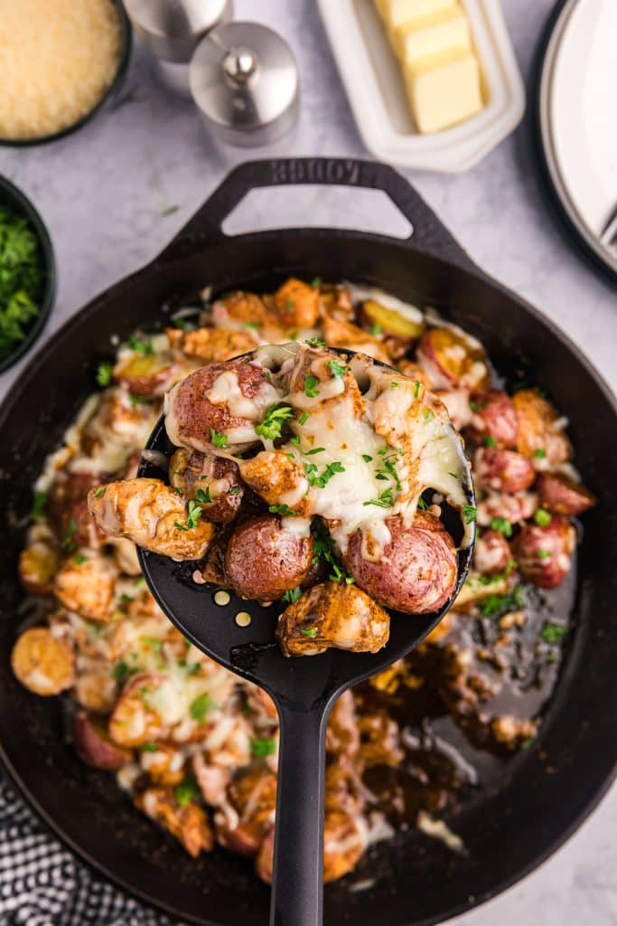spoon lifting a scoop of chicken & potatoes from a skillet.