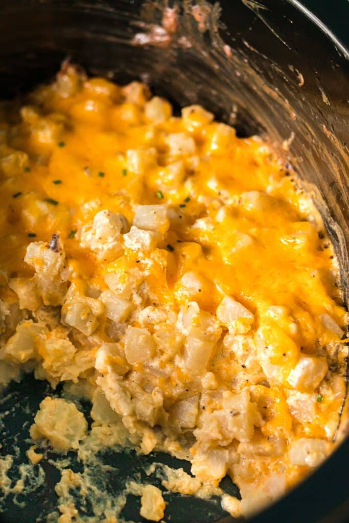 cheesy potatoes in a black crockpot.