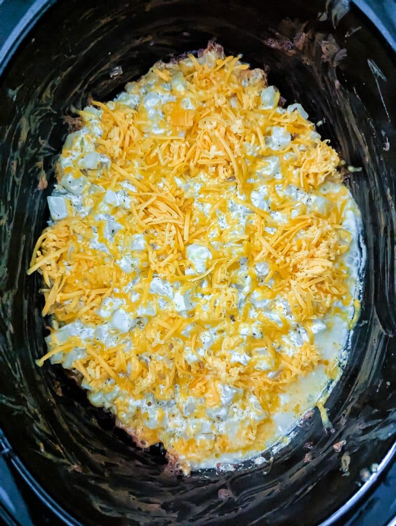 overhead shot of shredded cheddar sprinkled in a slow cooker.
