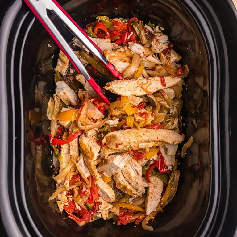 tongs in a slow cooker with chicken fajitas.