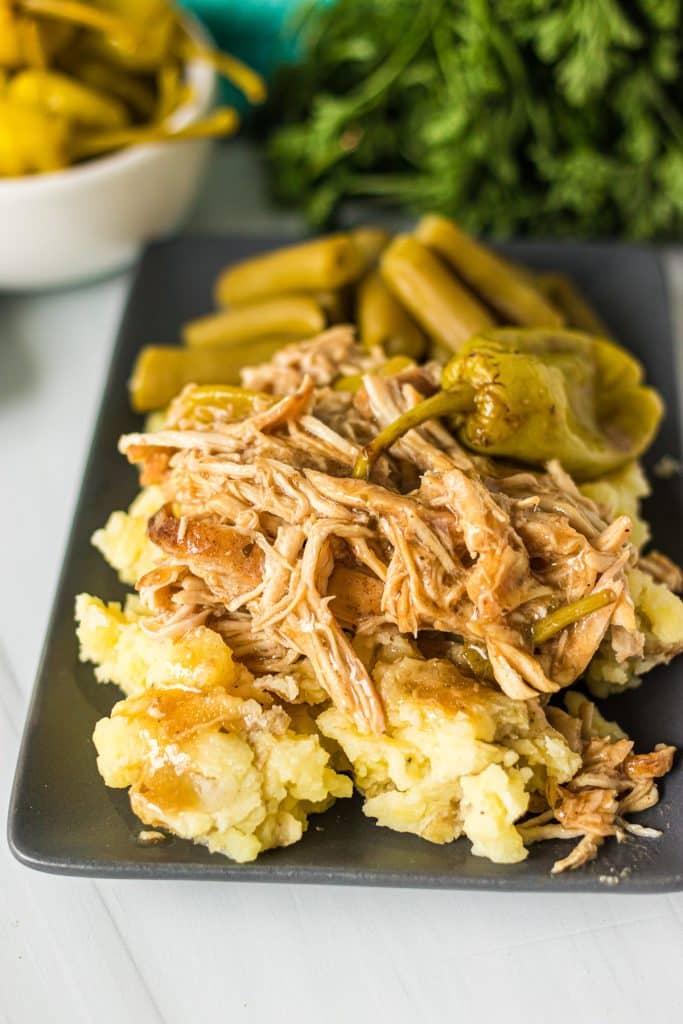 plate with mashed potatoes topped with mississippi chicken and green beans.