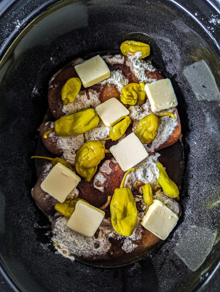 overhead shot of chicken, butter, and seasonings in a crockpot.