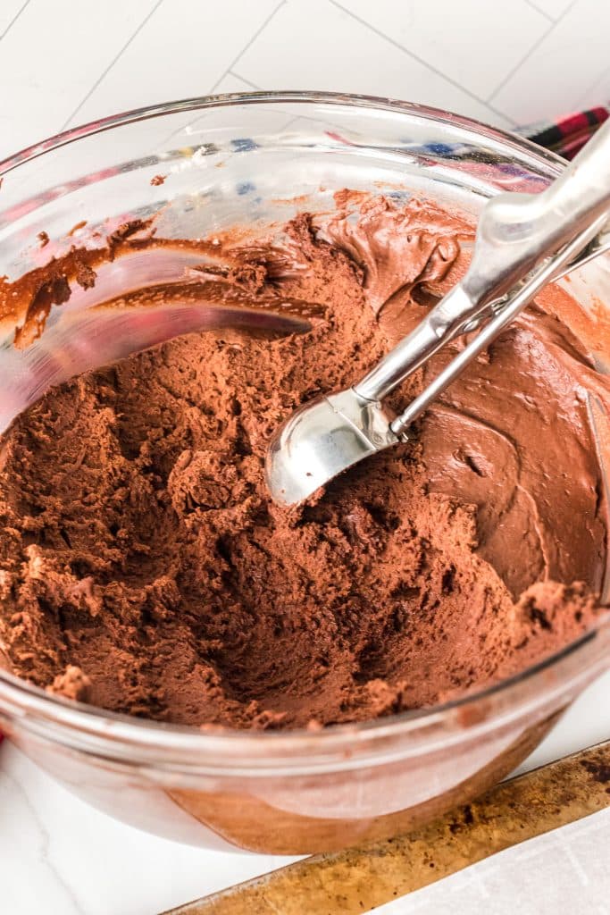 chocolate cookie dough in a mixing bowl with a cookie scoop.