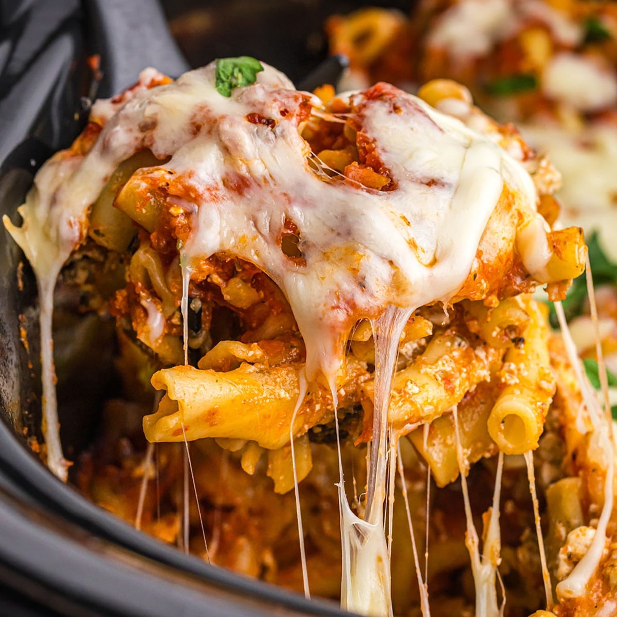 spoon lifting cheesy ziti from a slow cooker.