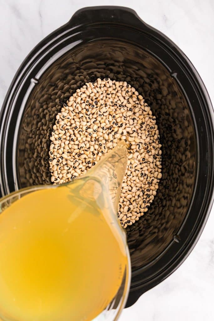 chicken broth pouring into a crockpot of peas.