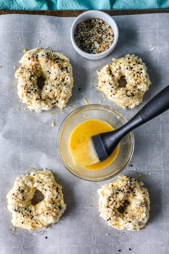 overhead shot of egg wash going onto bagels.