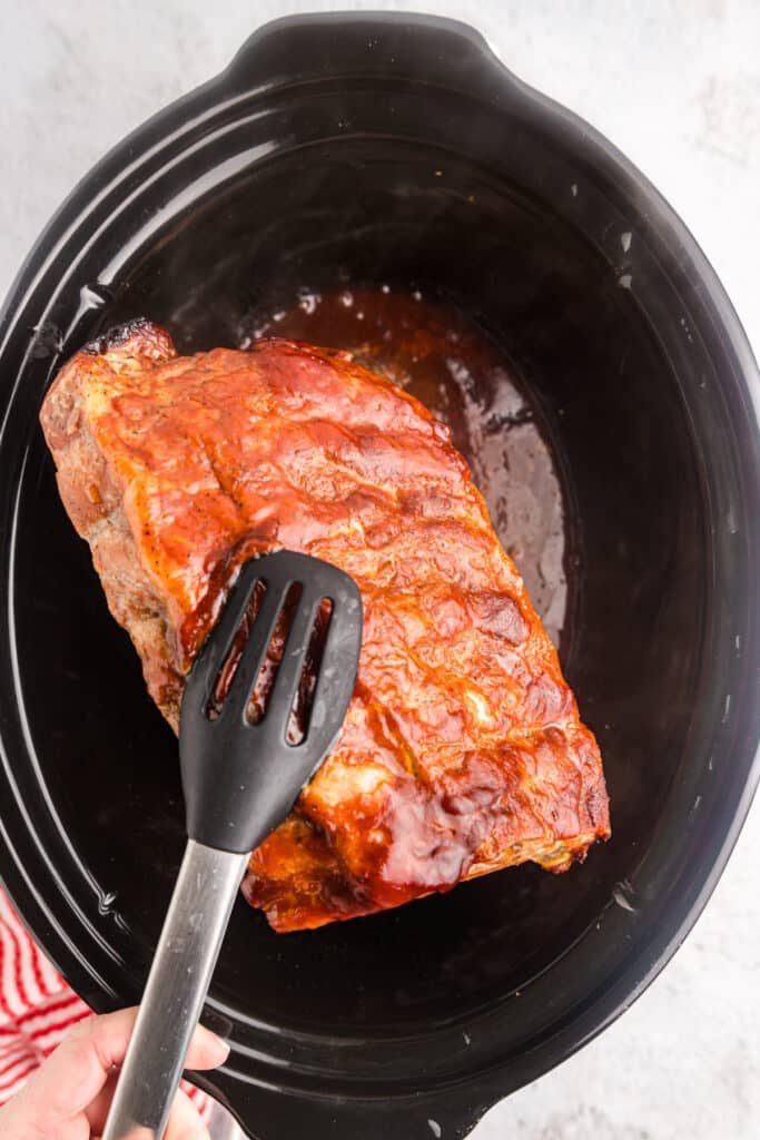 tongs lifting ribs from a crockpot.