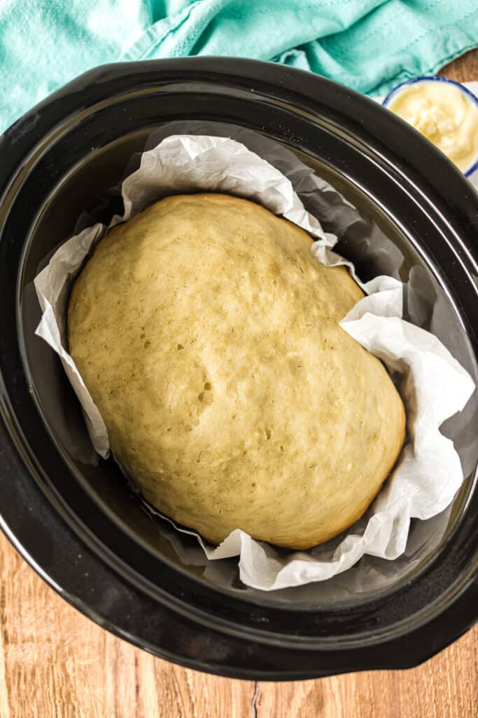 overhead shot of loaf of bread in parchment paper in a slow cooker.