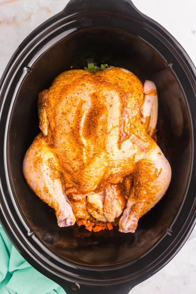 raw chicken rubbed with seasonings in a slow cooker.