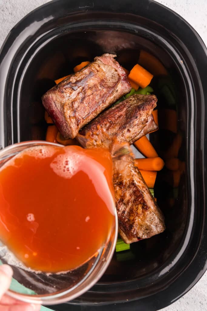 sauce pouring into a crockpot with short ribs.