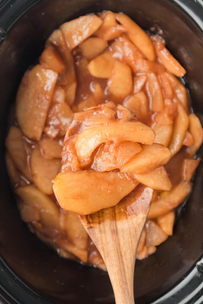 wooden spoon lifting a scoop of apples from a slow cooker.