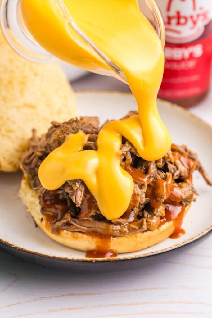 cheddar cheese sauce pouring over a beef sandwich.