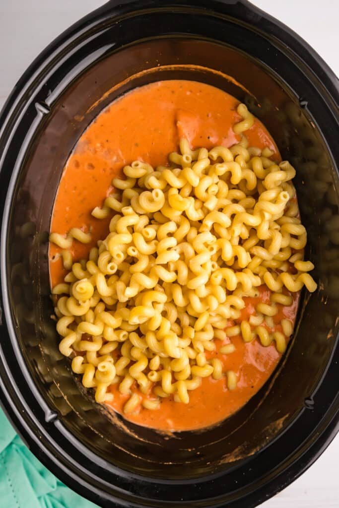 cavatappi noodles poured into creamy sauce in a crockpot.