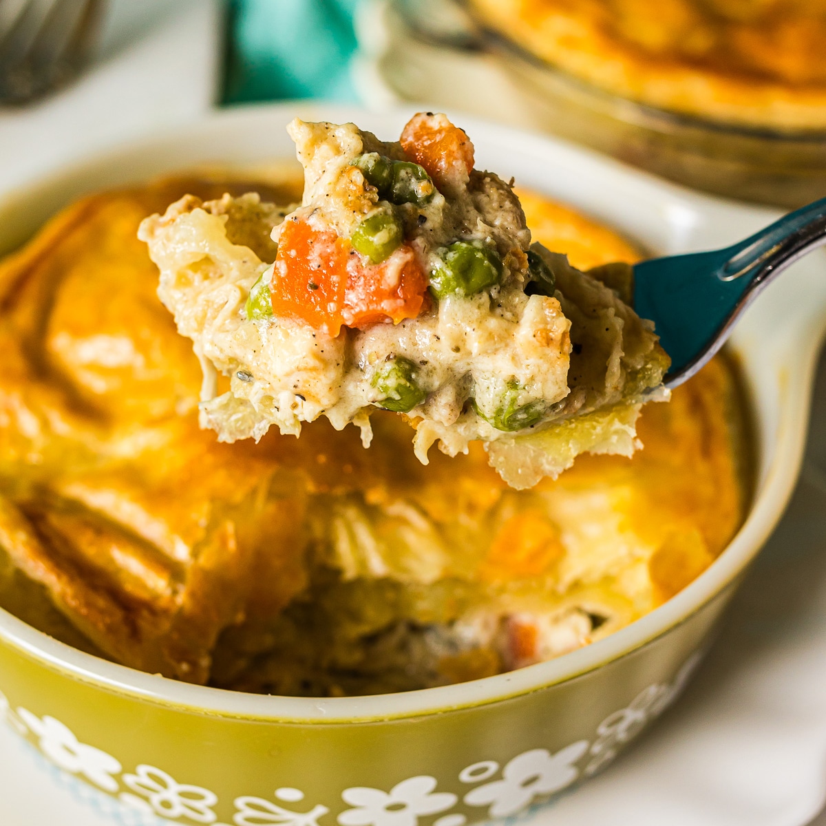 fork lifting a bite of chicken pot pie from a pyrex dish.