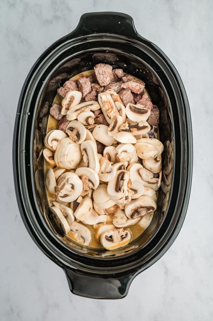 overhead shot of mu sliced mushrooms in a crockpot.