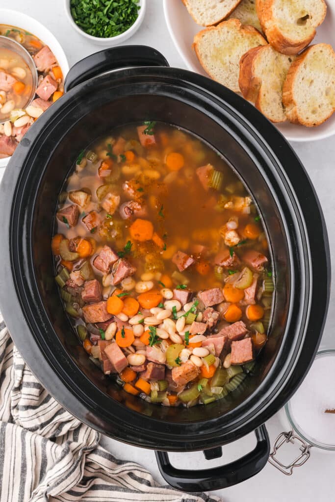overhead shot of ham and bean soup in a black crockpot.