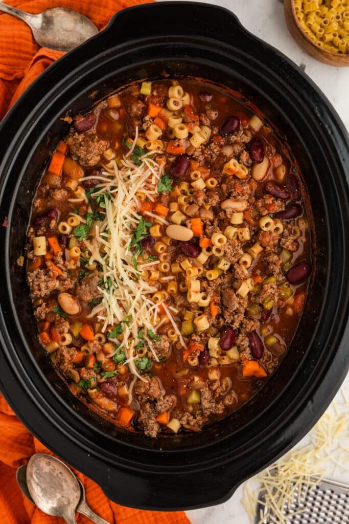 overhead shot of pasta fagioli in a slow cooker topped with parmesan cheese.