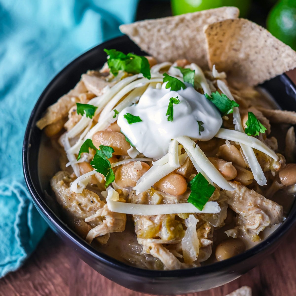 bowl of white chicken chili topped with cheese, cilantro, and tortilla chips.