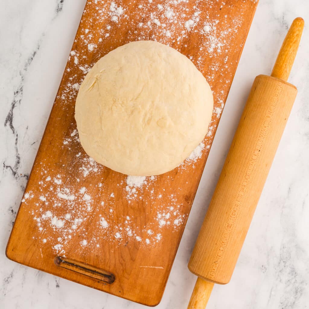 ball of dough on a floured board next to a rolling pin.