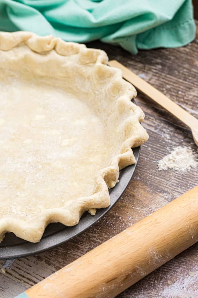 side view of crimped pie crust in a plate next to a rolling pin.
