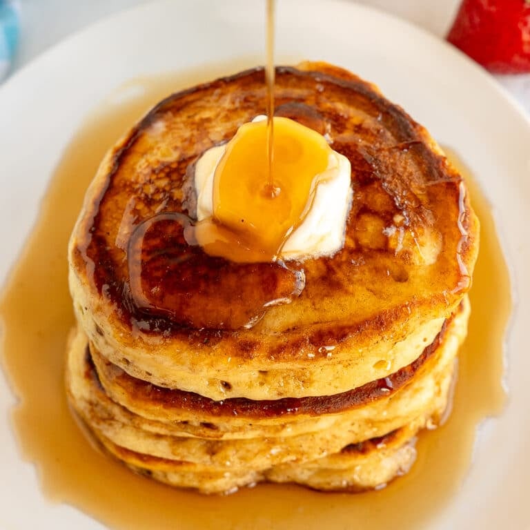 syrup drizzling over a stack of buttered pancakes.