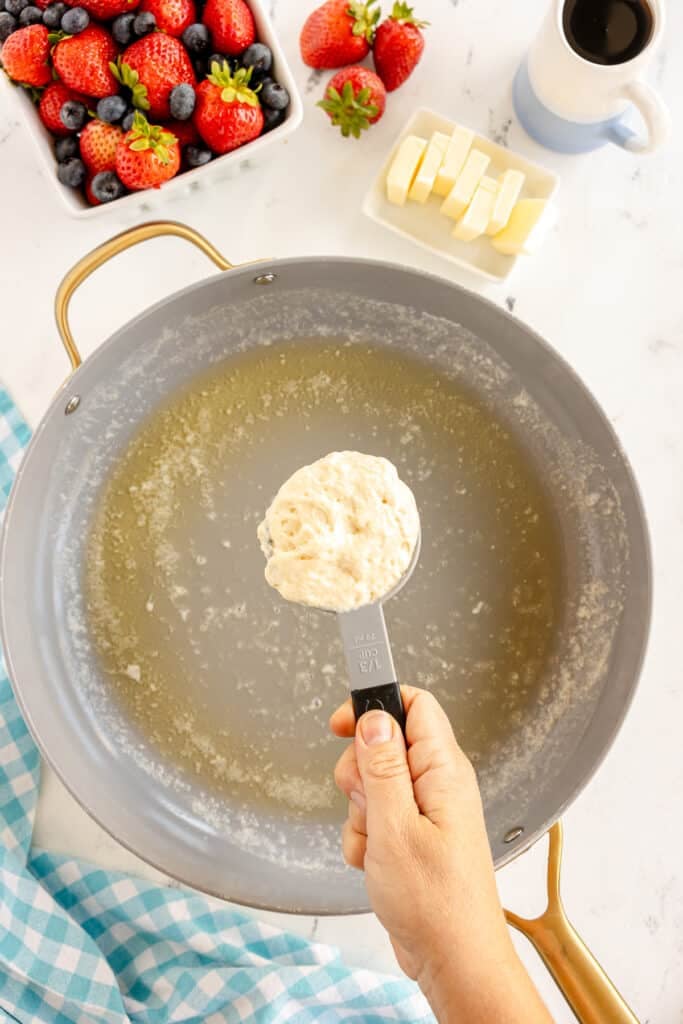 a measuring spoon portioning pancake batter over a buttered skillet.