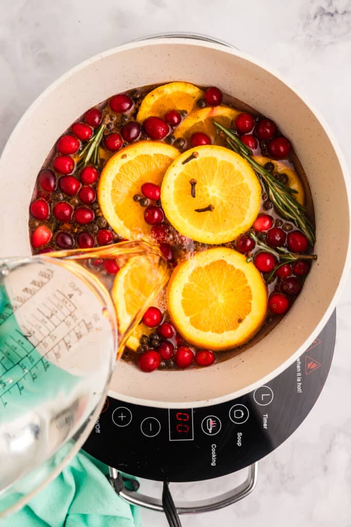 water pouring into a pot of oranges, cranberries, and spices.
