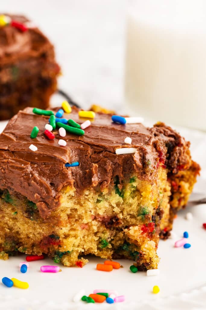 Slice of colorful sprinkle cake with chocolate frosting with a bite missing.