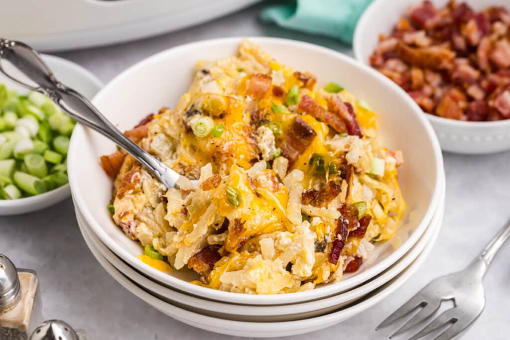 A bowl of hash brown casserole garnished with bacon and scallions.